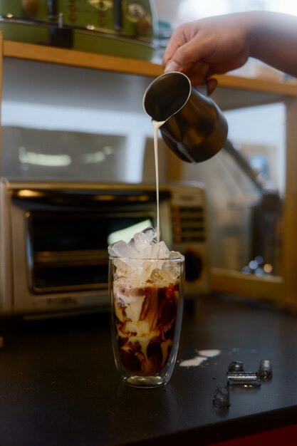 Barista gießt Milch über Kaffee in Glas