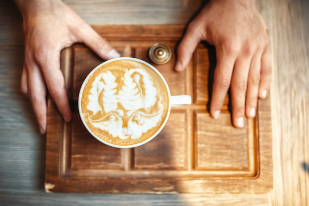 Barista hält eine Tasse Kaffee mit Schaumzeichnung