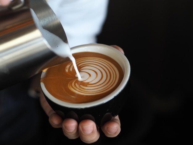 Barista-Hände, die warme Milch für die Herstellung von Kaffee Latte Art gießen.