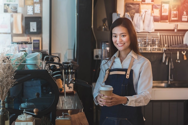 El barista hermoso joven asiático de la mujer lleva el delantal azul