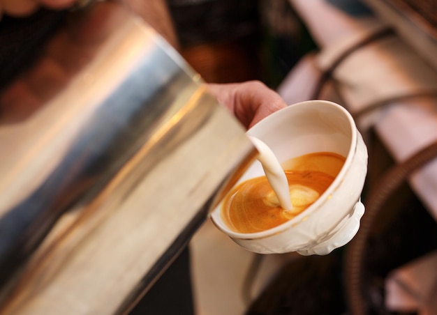 Barista in der Kaffeebar, der den richtigen Cappuccino zubereitet und aufgeschäumte Milch in eine Tasse Kaffee gießt, um Latte-Art-Muster zu erstellen Professionelles Catering-Konzept