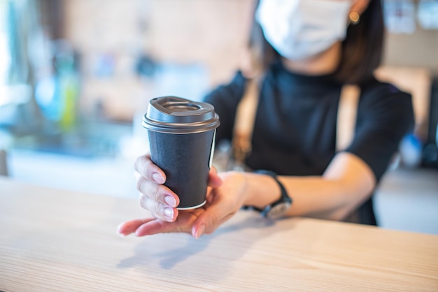 Barista in Schürze und Gesichtsmaske hinter der Theke, bereit, Kaffeeservice im Geschäft zu geben