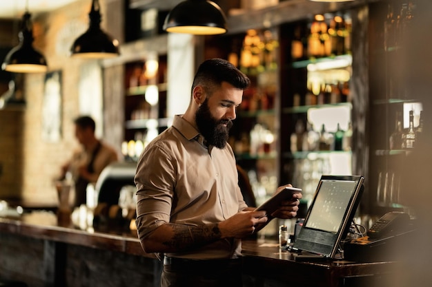 Barista joven que usa el panel táctil mientras está parado en la caja registradora en un bar.