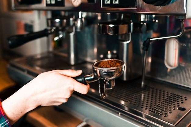 Barista lleva un recipiente con café molido a una cafetera