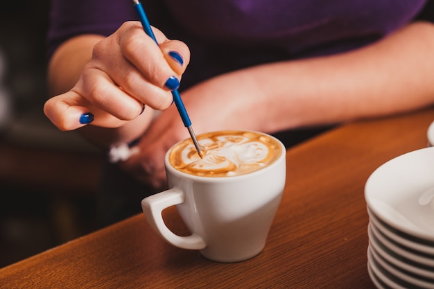 Barista macht eine Tasse Latte-Art-Kaffee mit speziellem Metallgerät - Latte-Art-Stiftwerkzeug