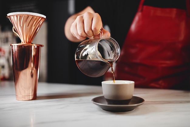 Barista macht einen tropfkaffee und gießt heißes wasser aus dem wasserkocher über einen kaffee