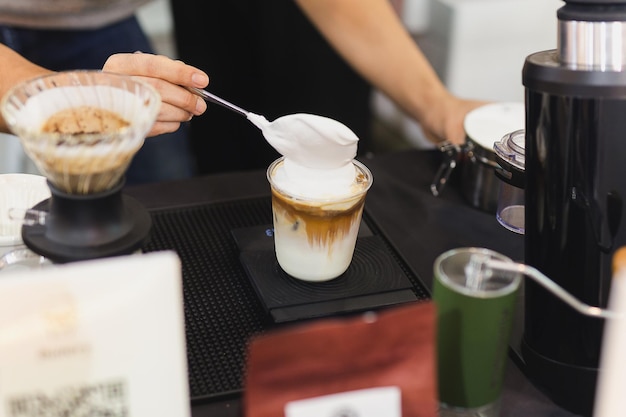 Barista macht Latte-Eiskaffee mit handgekröntem Auspeitschen im Café