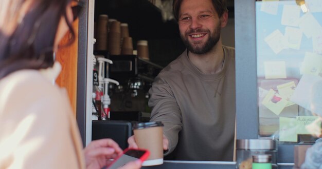 Foto barista-mann macht kaffee zum mitnehmen für eine kundin, die per kontaktlosem mobiltelefon an das kreditkartensystem zahlt