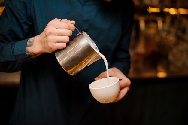 Barista manos vertiendo un poco de leche en una taza de café