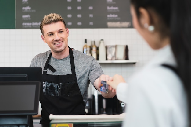 Barista masculino em pé no balcão do bar pegando cartão de crédito de uma cliente para pagar um café na cafeteria