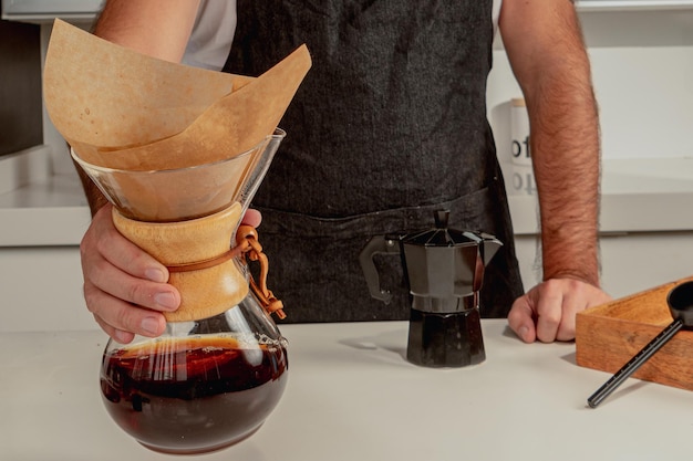 Barista masculino está haciendo café negro en la cafetera chemex, parado frente a la cafetería