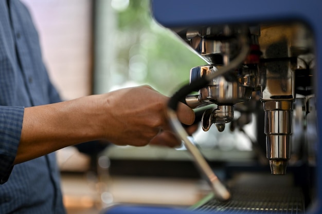 Un barista masculino que usa un portafiltro para hacer un trago de espresso con una máquina de café espresso