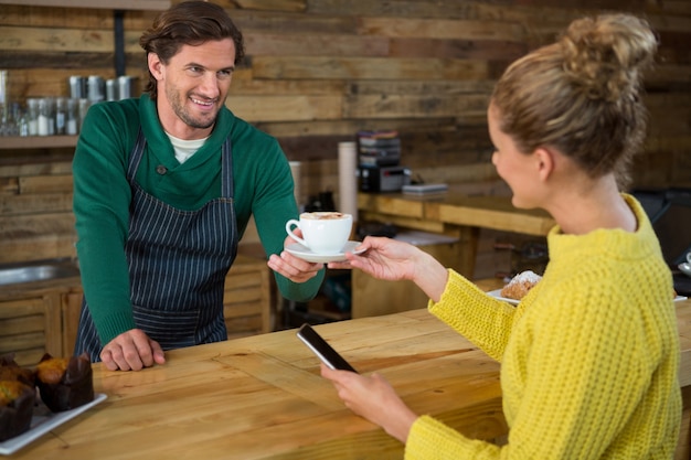 Foto barista masculino sonriente que sirve café a la clienta en la cafetería