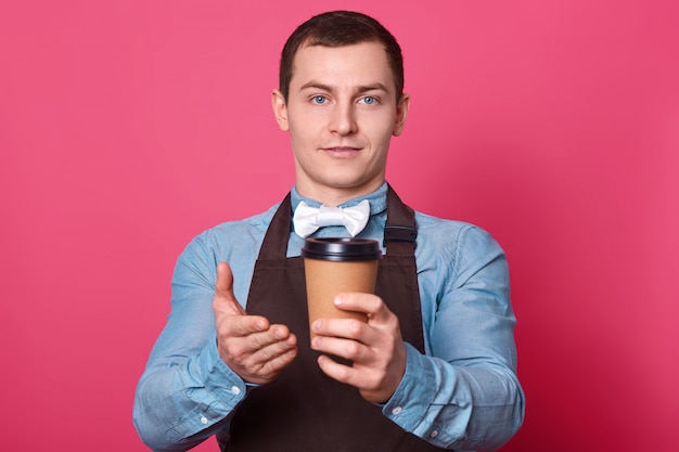 El barista masculino le sugiere que pruebe el café aromático hecho por él, muestra con una taza de bebida caliente desechable de palma