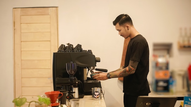 Barista masculino con tatuajes haciendo café con una máquina de café