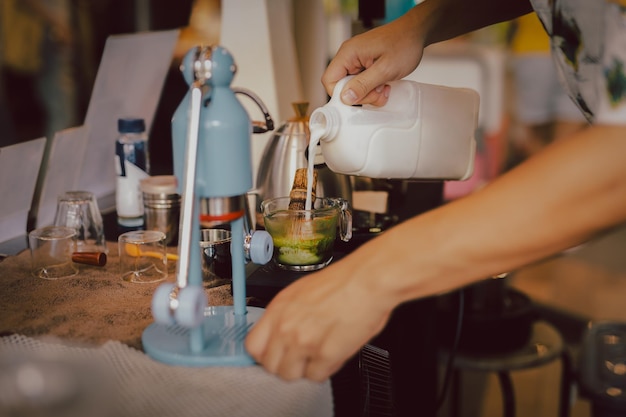 Foto barista preparando matcha latte com a mão derramando leite no café