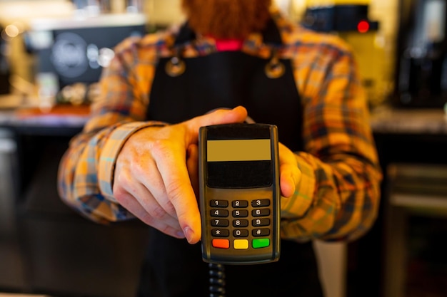 Barista profesional joven barbudo de jengibre pelirrojo con delantal negro trabajando en una cafetería