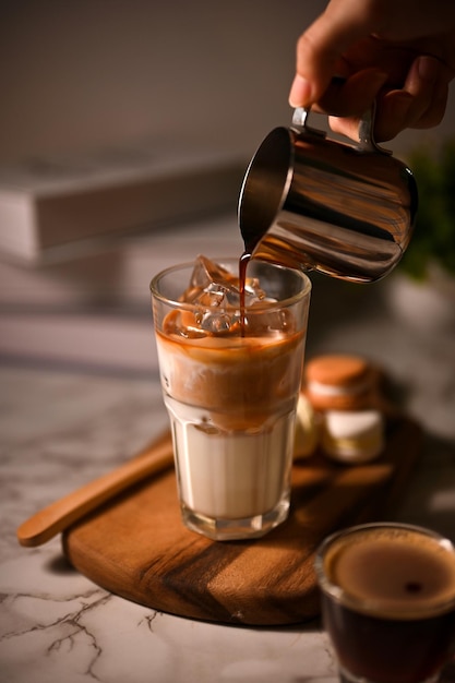 Un barista profesional que vierte un café oscuro en un vaso de leche con hielo