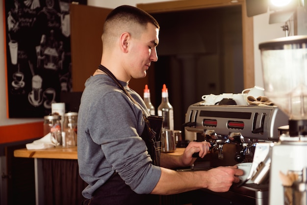 Barista profissional segurando o leite de aquecimento jarro de metal usando a máquina de café.