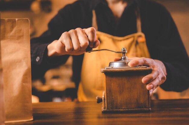 Barista segurando o moedor de mão para fazer bebidas moendo grãos de café torrados para bebida de cafeína no fundo do café da cozinha preparação do moinho de café da manhã com equipamento de café expresso em tom marrom