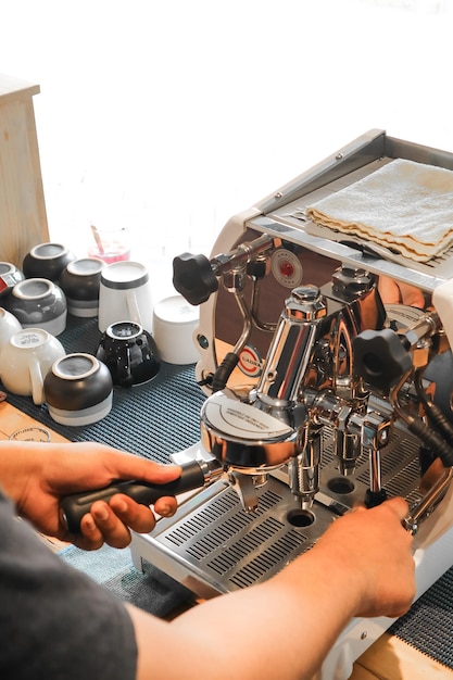 Barista segurando porta-filtro de suporte de café com café moído perto da máquina de café expresso profissional