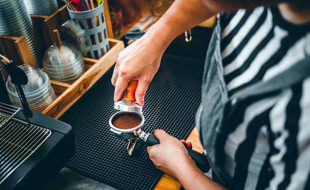 Barista segurando porta-filtro e tamper de café fazendo um café expresso no café