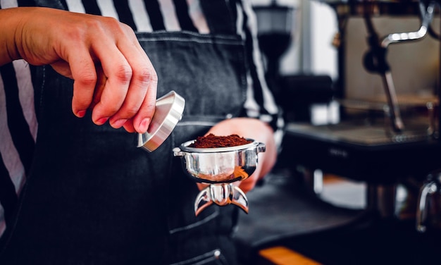 Barista segurando porta-filtro e tamper de café fazendo um café expresso no café