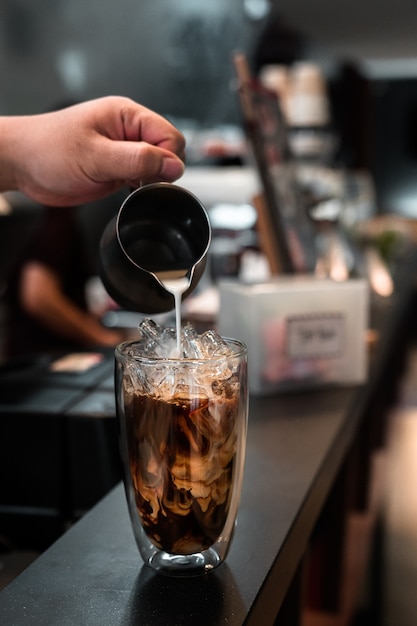 Barista servindo leite em um copo de café gelado