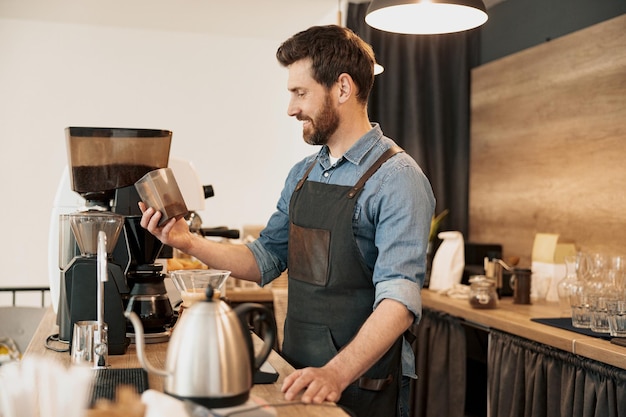 Barista sonriente vierte granos de café en el tanque de la máquina de café para moler en la cafetería