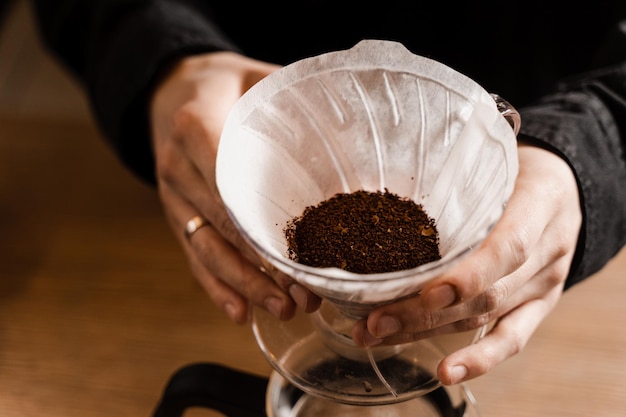 Barista sosteniendo el dispositivo de vertido con café molido en el filtro de papel antes de verter agua de la tetera de goteo