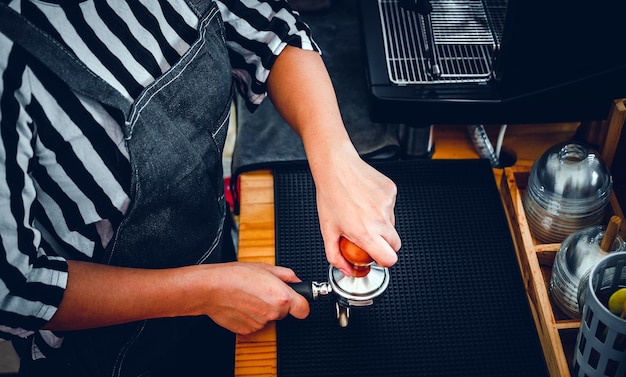 Barista sosteniendo un portafiltro y un tamper de café haciendo un café expreso en la cafetería