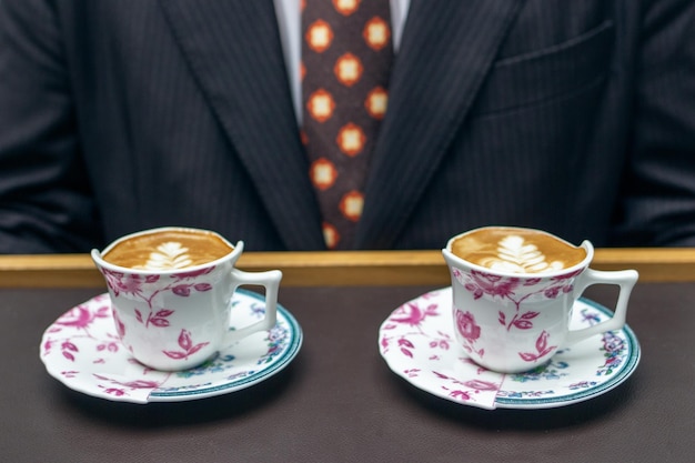 Foto barista sostiene dos cafés lateados und tazas de diseno