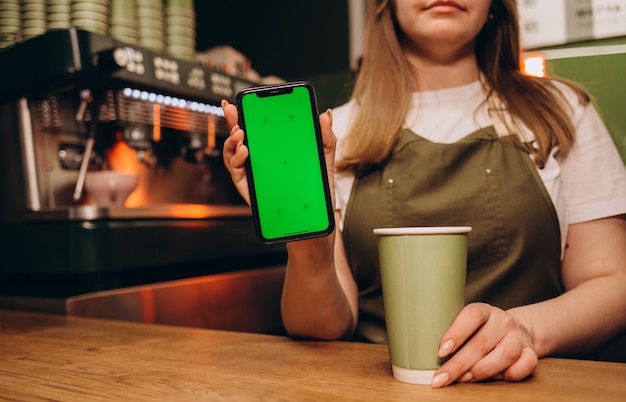 Barista sostiene un teléfono con pantalla verde en una taza de café