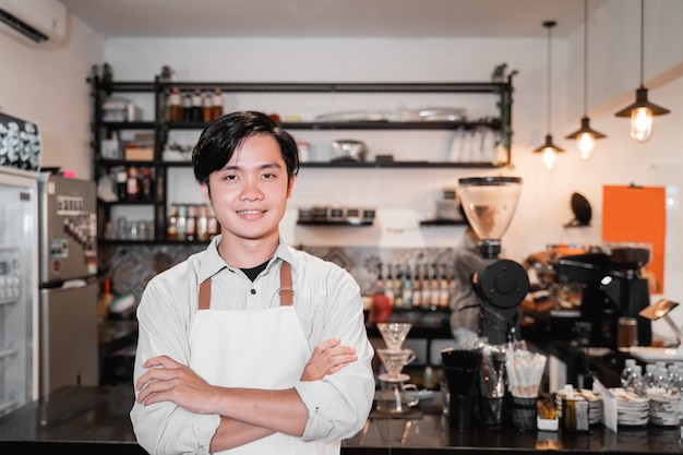 Barista steht mit gekreuzten Händen vor einem Café bei ihrer Arbeit