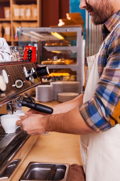 Barista en el trabajo. Vista lateral del confidente barista haciendo café mientras está de pie en la barra del bar cerca de la máquina de café