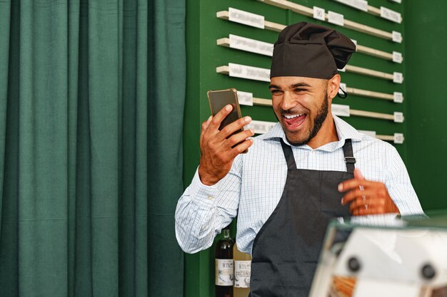 Barista usando su teléfono inteligente y riendo mientras está de pie en la cafetería.