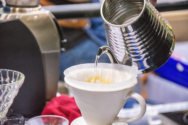 Barista verschüttet heißes Wasser und bereitet gefilterten Kaffee aus einer silbernen Teekanne zu