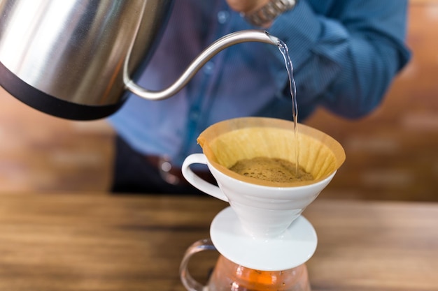 Barista vertiendo agua en el café con filtro en la cafetería.