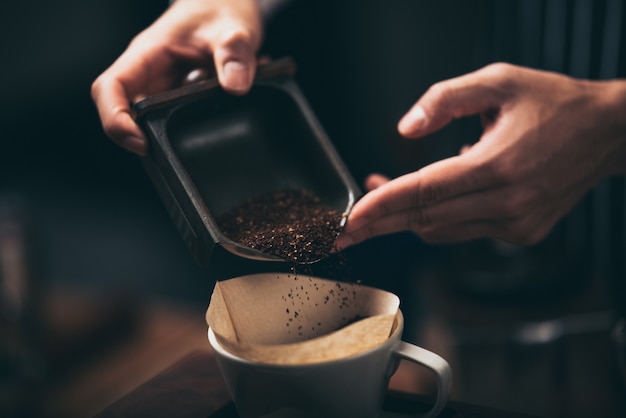 Barista vertiendo café en polvo de un molinillo de café a un gotero para hacer café recién hecho en la cafetería.