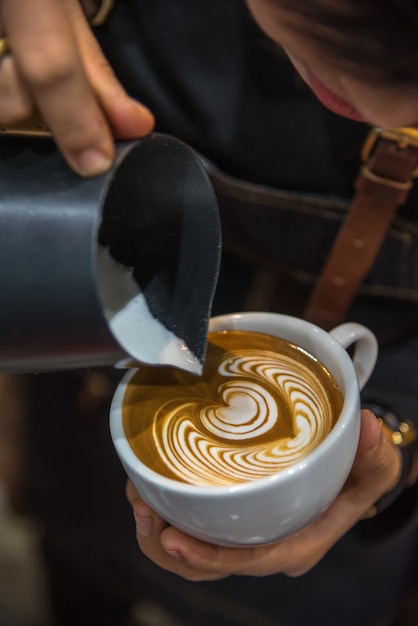 Barista vertiendo espuma de latte para hacer un café con leche en la taza de café con leche