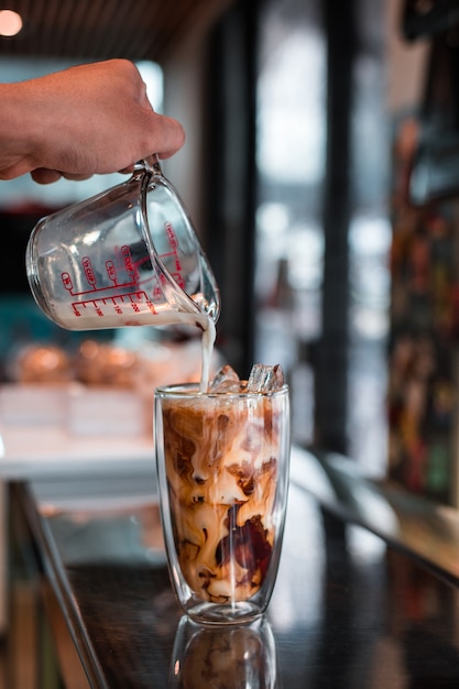 Barista vertiendo leche en un vaso de café helado