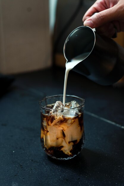 Barista vertiendo leche en un vaso de café helado