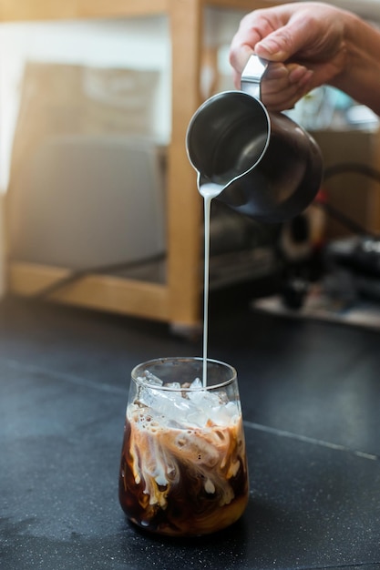 Barista vertiendo leche en un vaso de café helado