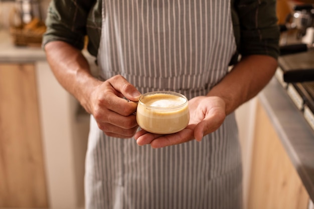 Barista vestindo avental listrado segurando xícara de cappuccino