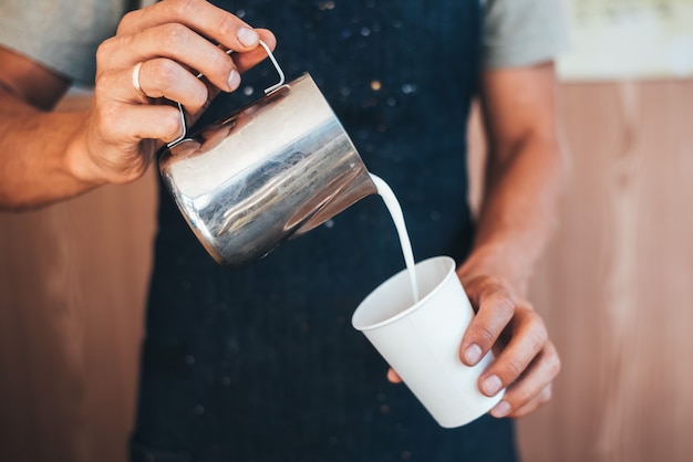 El barista vierte leche de una lata en café en un vaso desechable de papel.