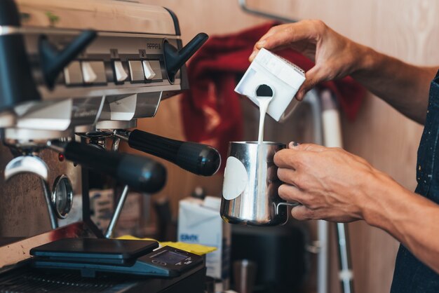 El barista vierte leche de una lata en café en un vaso desechable de papel.