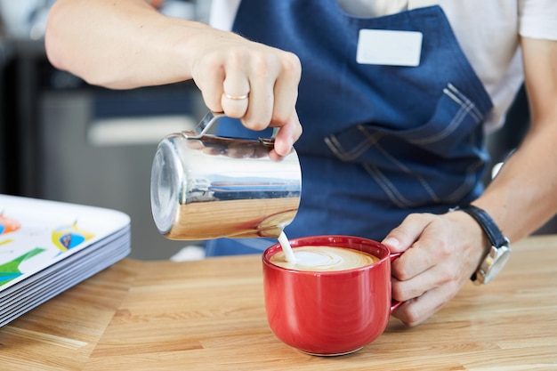 Baristas Hände gießen Milch in eine Tasse Cappuccino