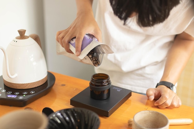 Baristas Hand legt Kaffeebohnen auf eine digitale Waage, um das Gewicht zu messen Leicht geröstet