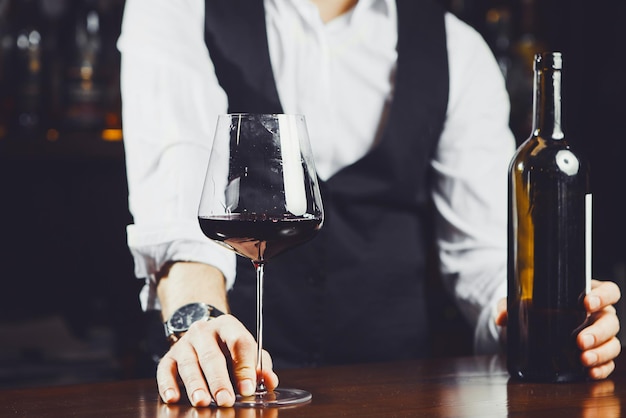 Barkeeper an der Bar mit Glas Rotwein und Flasche aus nächster Nähe