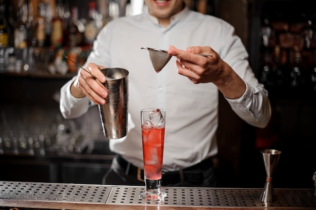 Barkeeper, der ein alkoholisches Getränk aus dem Stahlschüttler durch ein Sieb hinzufügt